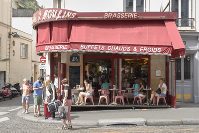 people sitting at outdoor dining tables under a red awning