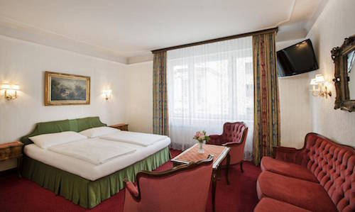 elegant hotel room with red furniture and green and white bed